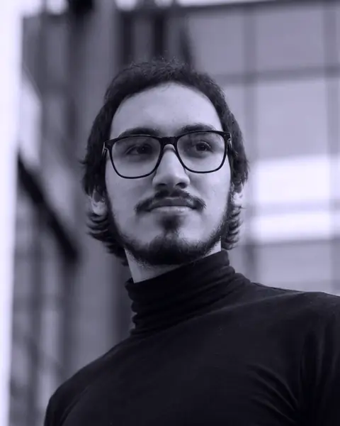 Retrato de Héctor Montero: con gafas y cuello alto negro, al aire libre, entre edificios.